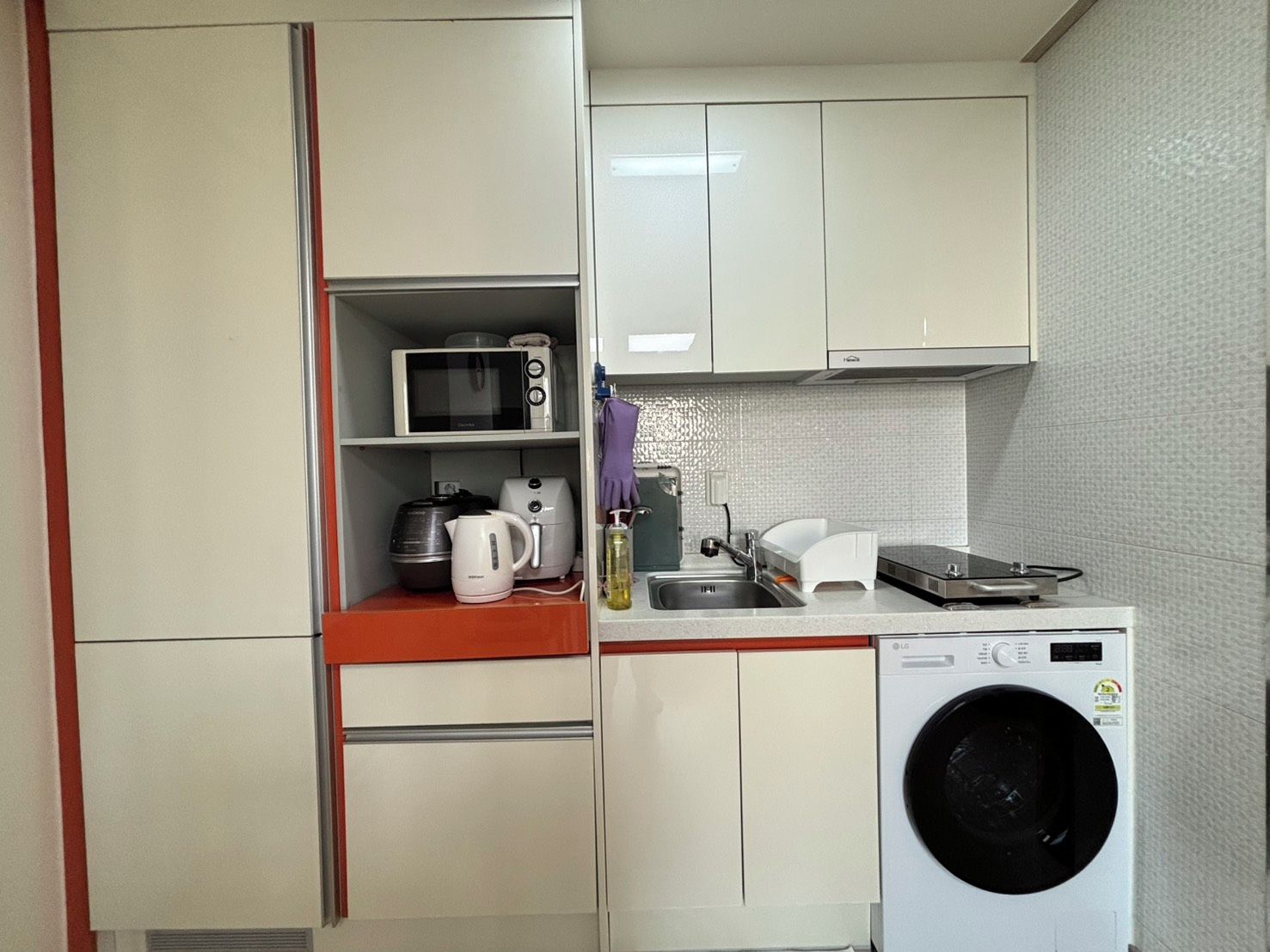Ett kompakt kök med mikrovågsugn, vattenkokare, brödrost och tvättmaskin.