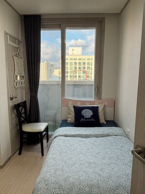 A bedroom with a bed, a chair, a window with a view of buildings, and a door.
