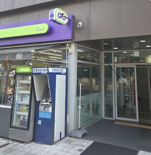 A building entrance with a glass door, a blue and white ATM, and a vending machine. - Ansan City View Balcony Apartment (Ansan-si)