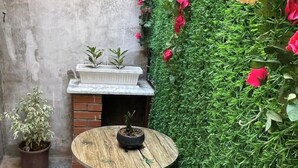 A small outdoor seating area with a round wooden table and metal chairs, a potted plant, and a green wall with flowers. - Studio in a house (Sétif)