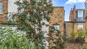 Un immeuble résidentiel aux murs de briques, avec une porte bien visible et un arbre aux fruits rouges.