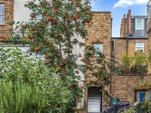 Un edificio residenziale con pareti in mattoni, una porta ben visibile e un albero con frutti rossi.