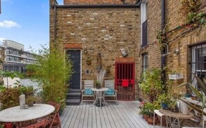 A courtyard with a brick wall, a door, a small table with chairs, and potted plants. - Artist Home Central London (London)