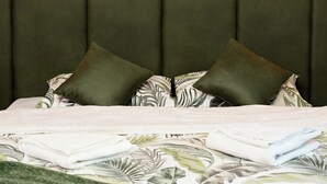 A bedroom with a large wall clock, a green upholstered headboard, and a bed with patterned bedding. - Brent Collection (Novi Sad)