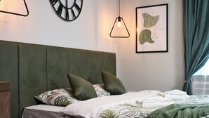 A neatly made bed with a green headboard, a pillow with a leaf pattern, and a framed artwork on the wall. - Brent Collection (Novi Sad)
