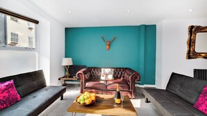 Una sala moderna con una pared de acento color turquesa, un sofá de cuero, una mesa de centro de madera con frutas y champán, y una decoración con cabeza de ciervo.