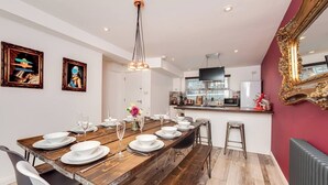 Un comedor con una larga mesa de madera dispuesta para seis personas, una cocina al fondo y una pared de acento roja.