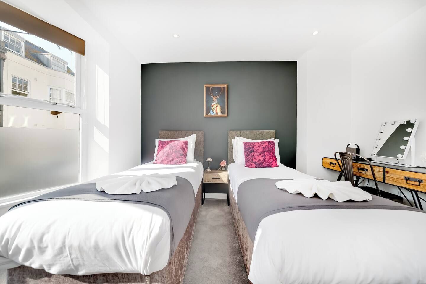 A hotel room with two beds, a desk with a mirror, and a painting on the wall.