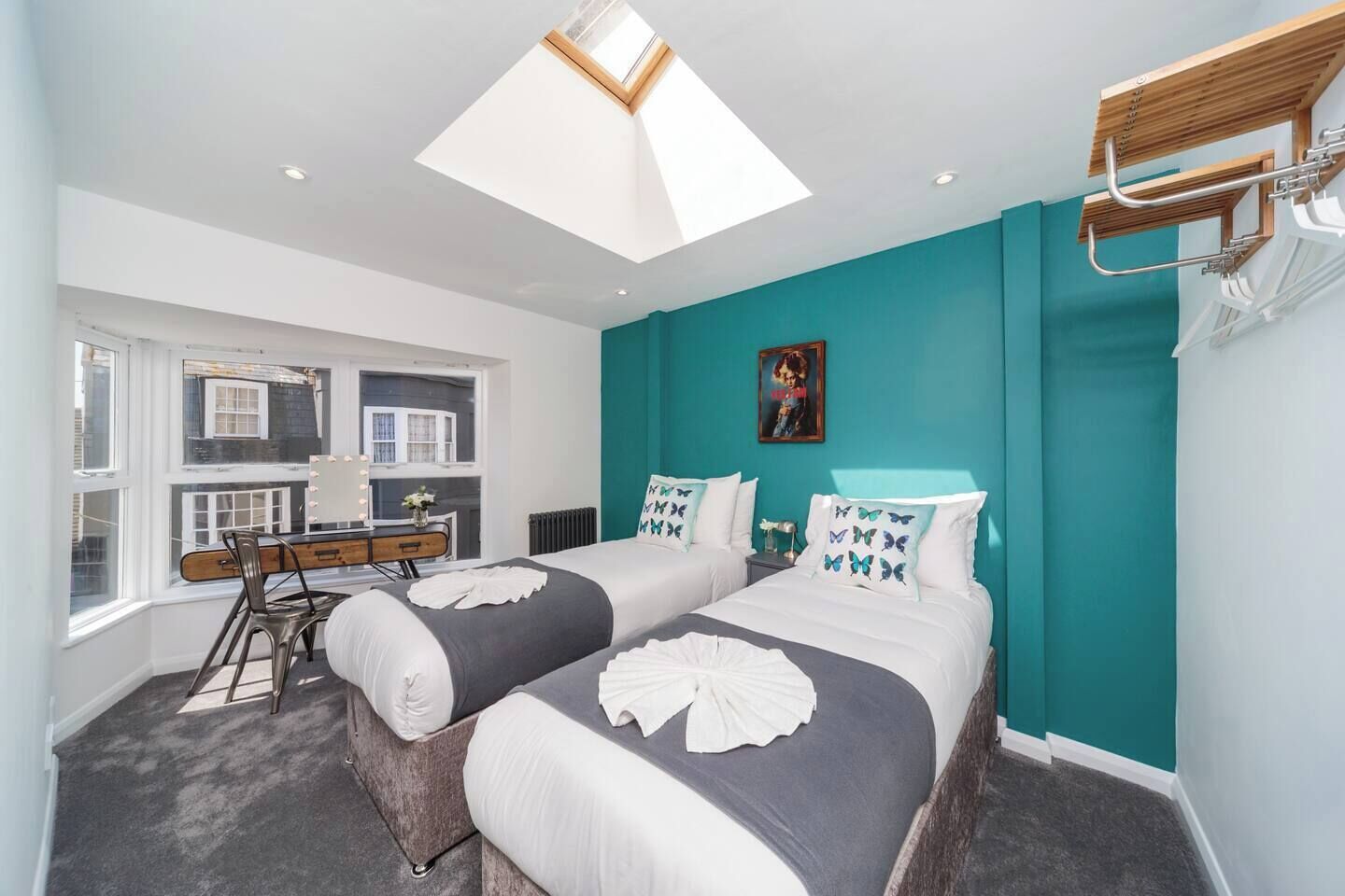 A modern bedroom with two beds, a vanity with a mirror, and a skylight.