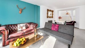 Una sala de estar moderna con una pared de acento color turquesa, un sofá de cuero, un sofá gris y una mesa de centro de madera con frutas y vasos.