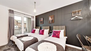 Habitación de hotel con dos camas, un ventanal con cortinas, una lámpara colgante y un perchero.