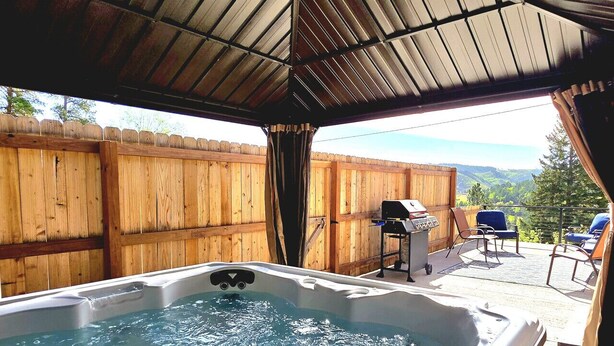 A hot tub under a covered patio with a wooden fence in the background. - Stunning, Spacious Mountain Home near Deadwood & 4X4 Trails (Lead)