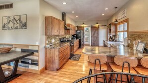 A spacious kitchen with wooden cabinets, a large island, and a dining area with chairs. - Stunning, Spacious Mountain Home near Deadwood & 4X4 Trails (Lead)