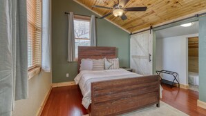 A bedroom with a wooden bed, a ceiling fan, a window with blinds, and a sliding barn door. - Stunning, Spacious Mountain Home near Deadwood & 4X4 Trails (Lead)