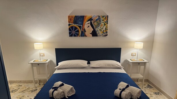 A hotel room with a large bed, two bedside tables, two lamps, and a painting on the wall. - Dimora del Tufo Antico - House in the heart of Avola (Avola)