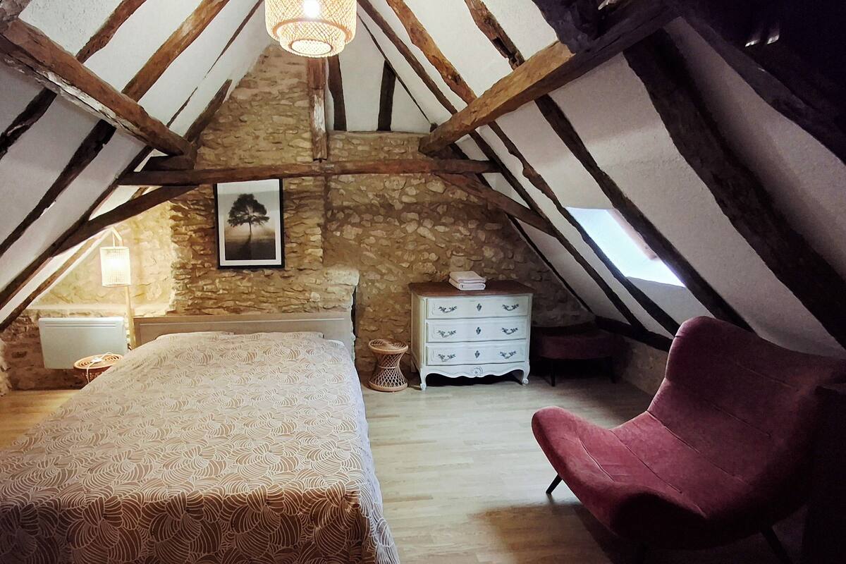 A bedroom with a bed, a chair, a dresser, and a stone wall.