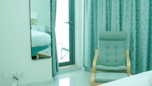 A hotel room with a bed, a chair, a mirror, and a window with curtains. - Zapbed House - LW 2007 (Dubai)