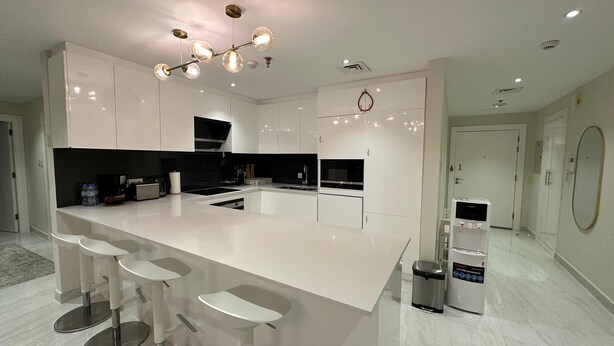 A modern kitchen with a central island, bar stools, a built-in oven, and a coffee machine. - Zapbed House - LW 2007 (Dubai)