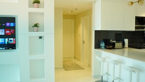 A modern kitchen with white cabinetry, a built-in TV, and a bar area with stools. - Zapbed House - LW 2007 (Dubai)