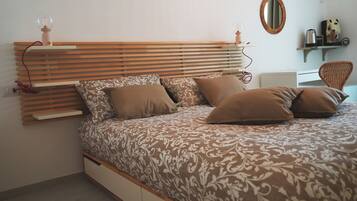Un dormitorio con cama, cabecera de madera, mesita de noche, lámpara, espejo y una silla.