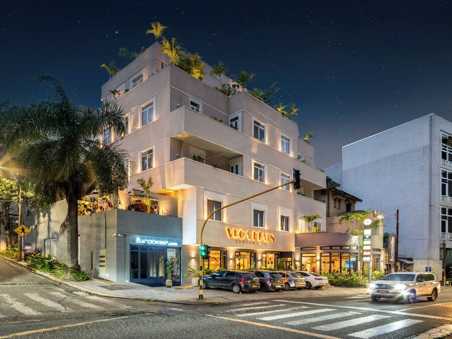 Un hotel de varios pisos con un diseño moderno, que cuenta con balcones con plantas y un restaurante visible llamado "VEGA FIALS".