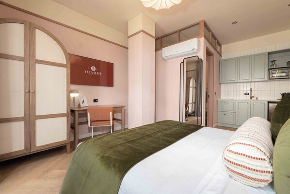 A hotel room with a bed, a desk, a chair, a wardrobe, and a kitchenette.
