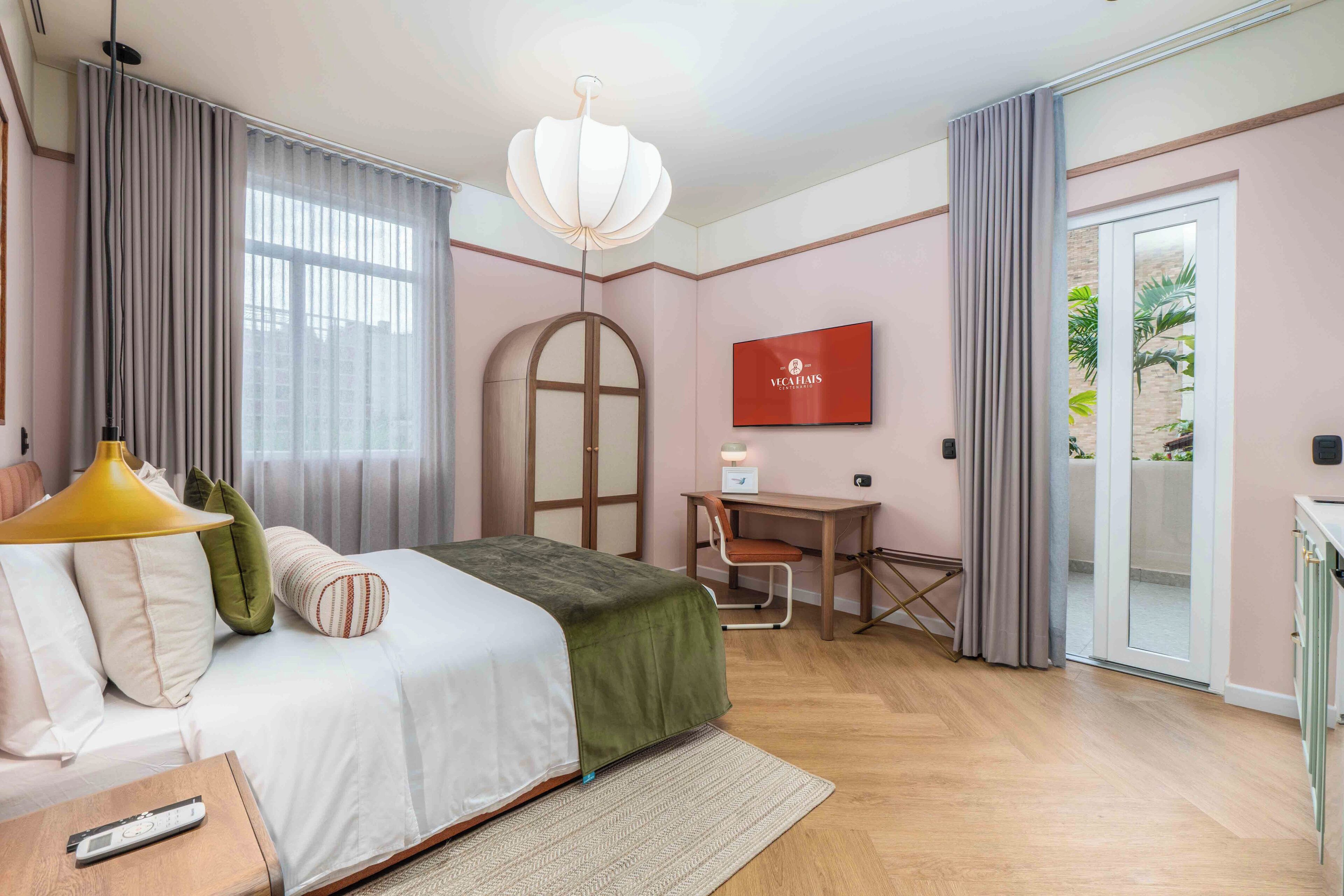Ein Schlafzimmer mit Bett, Nachttisch, Lampe, Fernseher, Schreibtisch, Stuhl und einer Schiebetür zum Außenbereich.
