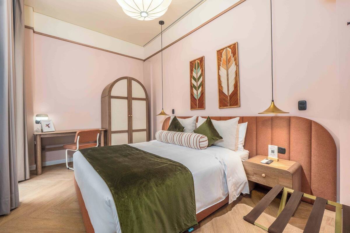 A neatly arranged hotel room with a bed, bedside table, desk, and chair.