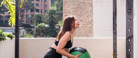 Una persona ejercita con una pelota medicinal en una azotea con vistas a edificios y árboles.