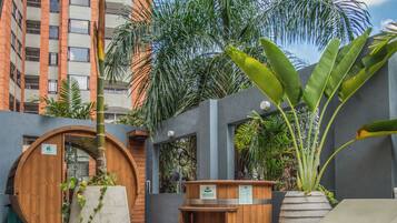 A wooden bench, a lounge chair, a wooden barrel, and a potted plant in an outdoor area with steps leading up to a building.