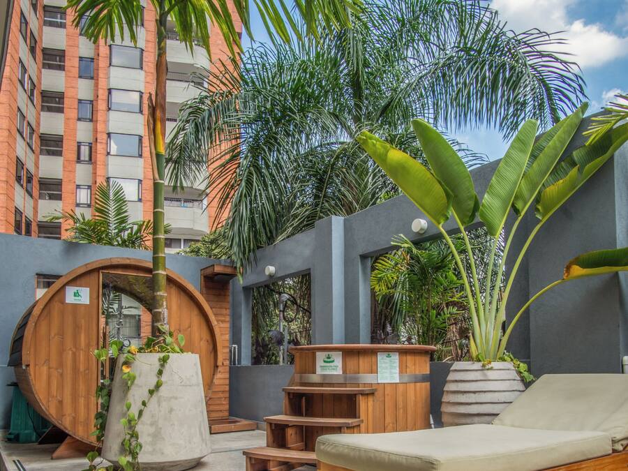 A wooden bench, a lounge chair, a wooden barrel, and a potted plant in an outdoor area with steps leading up to a building.
