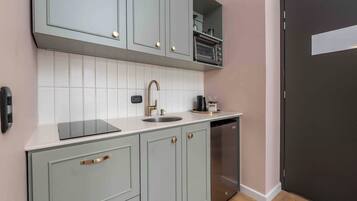 A kitchen with light green cabinets, a white countertop, a stainless steel sink, and a built-in oven.