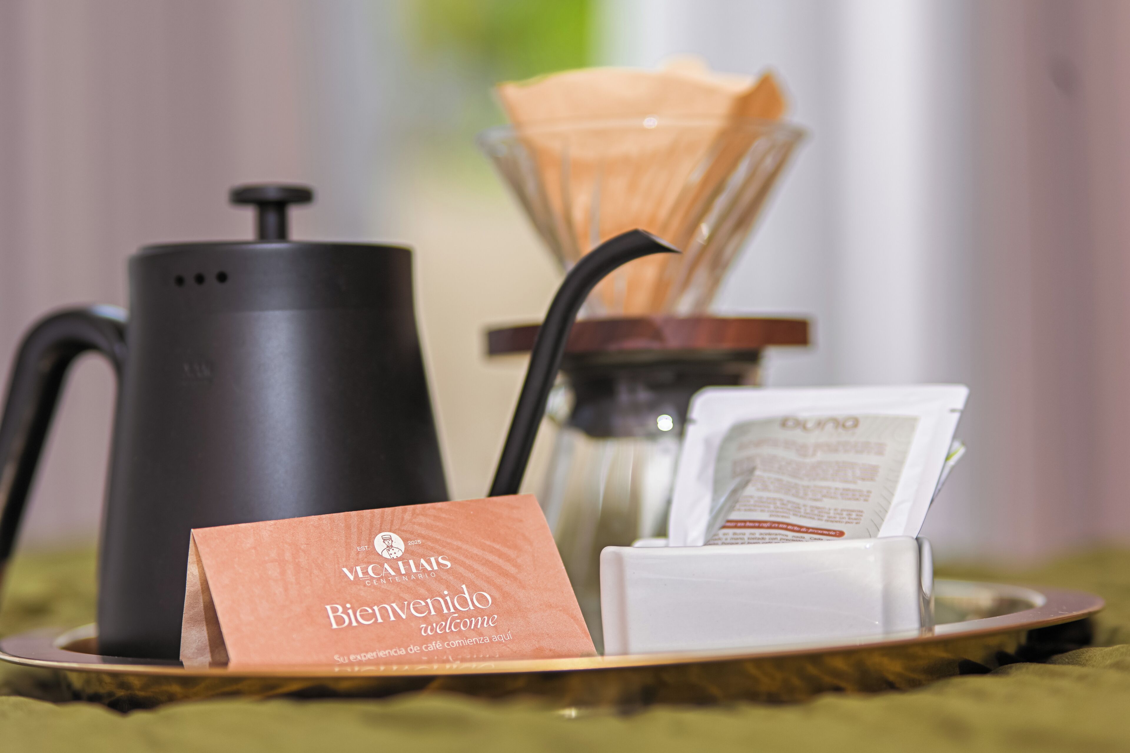 Une machine à café, un sac en papier avec l’inscription « Bienvenido », et un objet blanc sur un plateau.