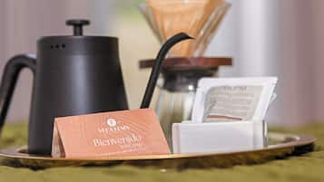 Eine Kaffeemaschine, eine Papiertüte mit dem Schriftzug 'Bienvenido' und ein weißes Objekt auf einem Tablett.