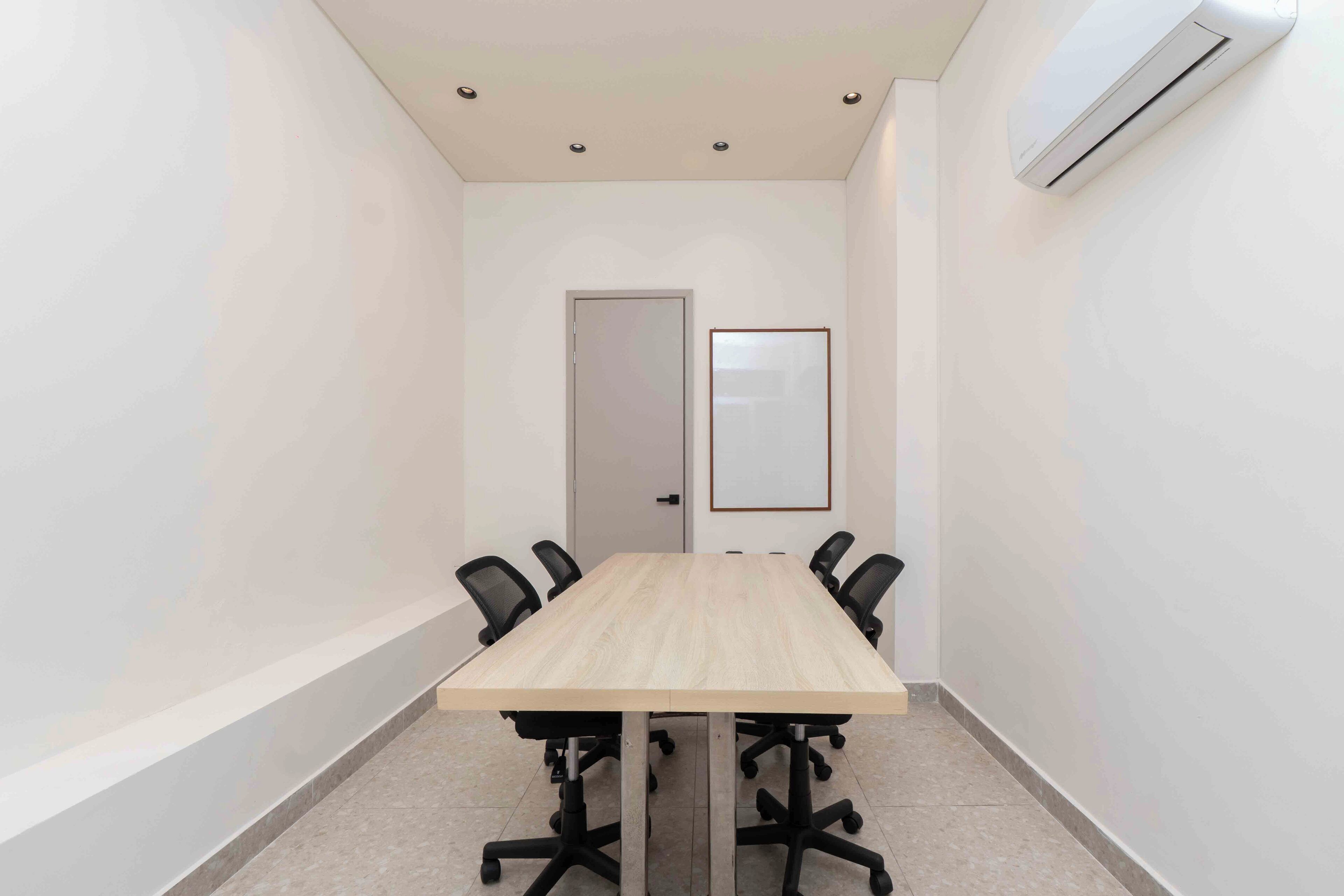 Une salle de conférence avec une longue table, des chaises de bureau noires, une porte et un climatiseur fixé au mur.