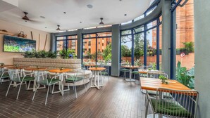 A modern indoor dining area with round tables and chairs, large windows, and indoor plants. - Veca Flats Centenario  (Cali)