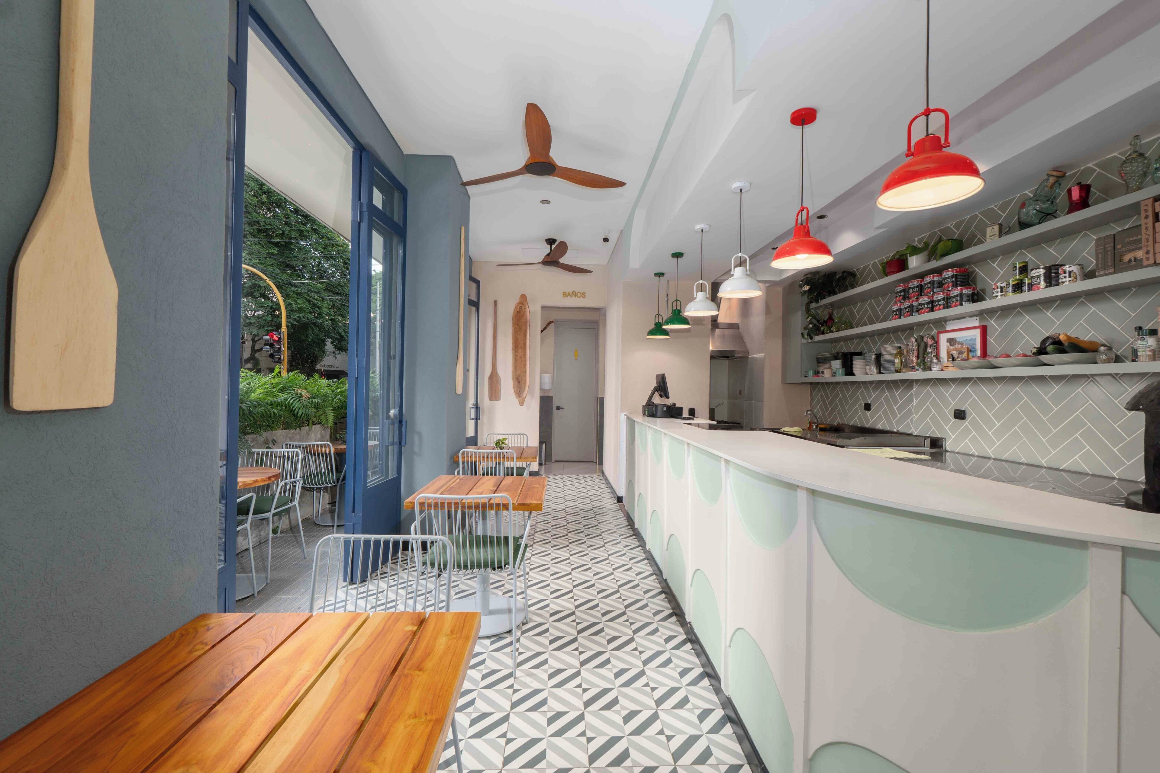 A modern kitchen with white cabinets, a herringbone tile floor, and red pendant lights.