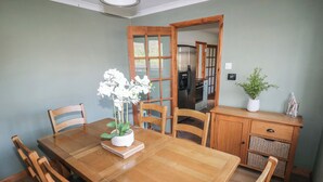 Un coin repas avec une table en bois, des chaises, une plante en pot et une cuisine en arrière-plan.