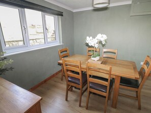 Een eethoek met een houten tafel en stoelen, een raam met zonwering en een klein plantje op de tafel.