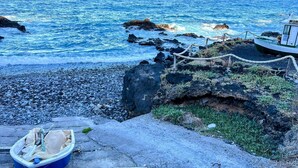 Une côte rocheuse avec un petit bateau amarré à un poteau et un panneau indiquant qu’il est interdit de s’y baigner.