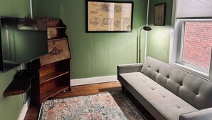 A room with a green wall, a framed architectural drawing, a wooden dresser, a grey sofa, and a window with a brick wall view. - Walkable near downtown 1 Bedroom (Portland)