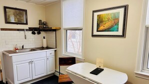 A kitchen with white cabinets, a wooden countertop, and a window with blinds. There is a framed painting on the wall and a small table with a chair. - Walkable near downtown 1 Bedroom (Portland)