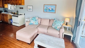 Un salon chaleureux avec un plafond en bois, un canapé beige, une table basse blanche et une cuisine en arrière-plan.