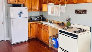 Une cuisine avec des armoires en bois, un réfrigérateur blanc, un four à micro-ondes, une cuisinière et une pancarte indiquant : « HOMARDS FRAIS DE MAINE ».