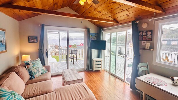 Un salon chaleureux avec un plafond en bois, un canapé, une table et une porte-fenêtre coulissante donnant sur un balcon.