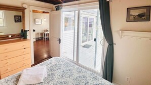 Une chambre à coucher avec un lit, un plafond en bois, des portes-fenêtres coulissantes donnant sur un balcon, une commode et un tableau encadré au mur.