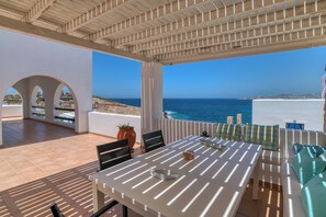 An outdoor patio with a table and chairs, a sofa, and a view of the sea.