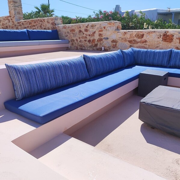 A modern outdoor seating area with a stone wall backdrop, a stone column, and a view of the surrounding landscape.