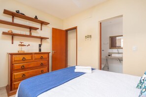 A bedroom with a bed, a wooden dresser, and a bathroom visible through an open door. - Bz74 Casa piscina e churrasqueira priv (Buzios)