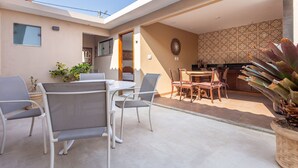 A patio with a table and chairs, a dining area with a wooden table and chairs, and a kitchen area with a patterned backsplash.